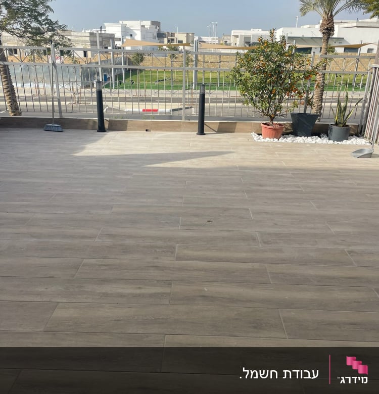 מרפסת עם מעקה מתכת, עציצים ועצים ברקע